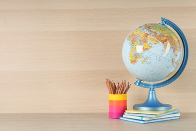Globe, books and school supplies on wooden table, space for text. Geography lesson