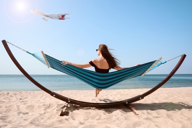 Image of Young woman relaxing in hammock on beach under blue sky with flying plane. Summer vacation