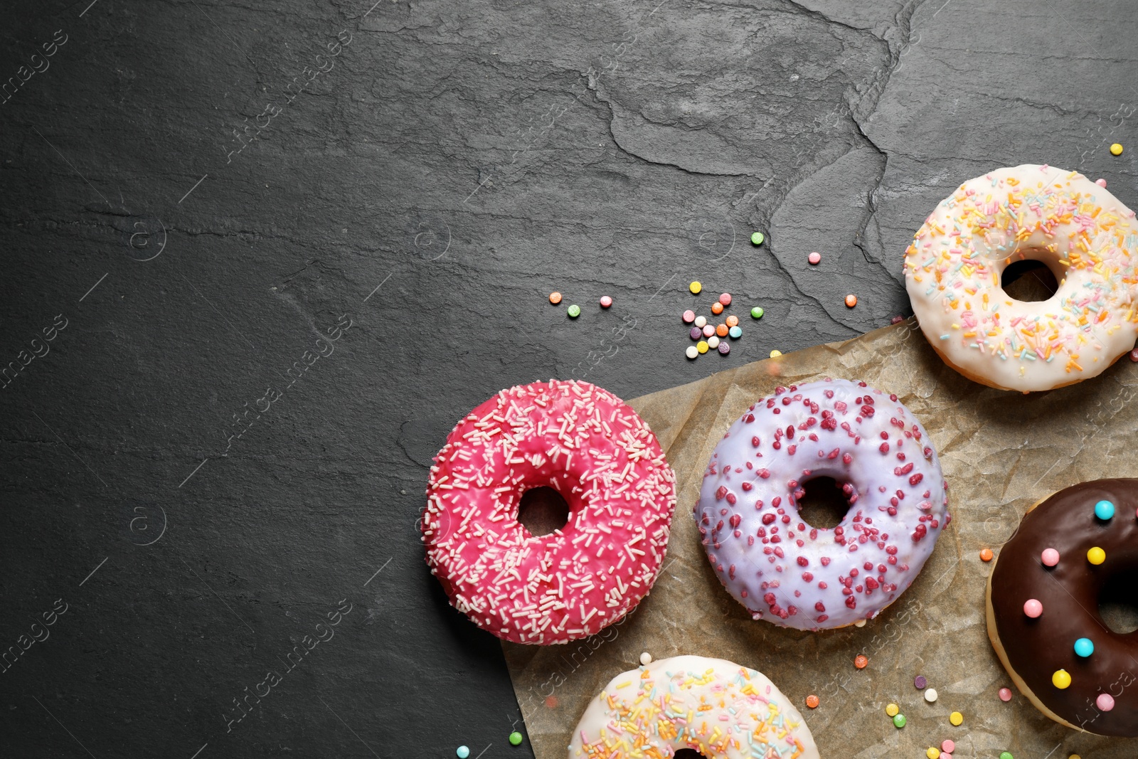 Photo of Yummy donuts with sprinkles on dark background, flat lay. Space for text