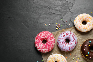 Photo of Yummy donuts with sprinkles on dark background, flat lay. Space for text