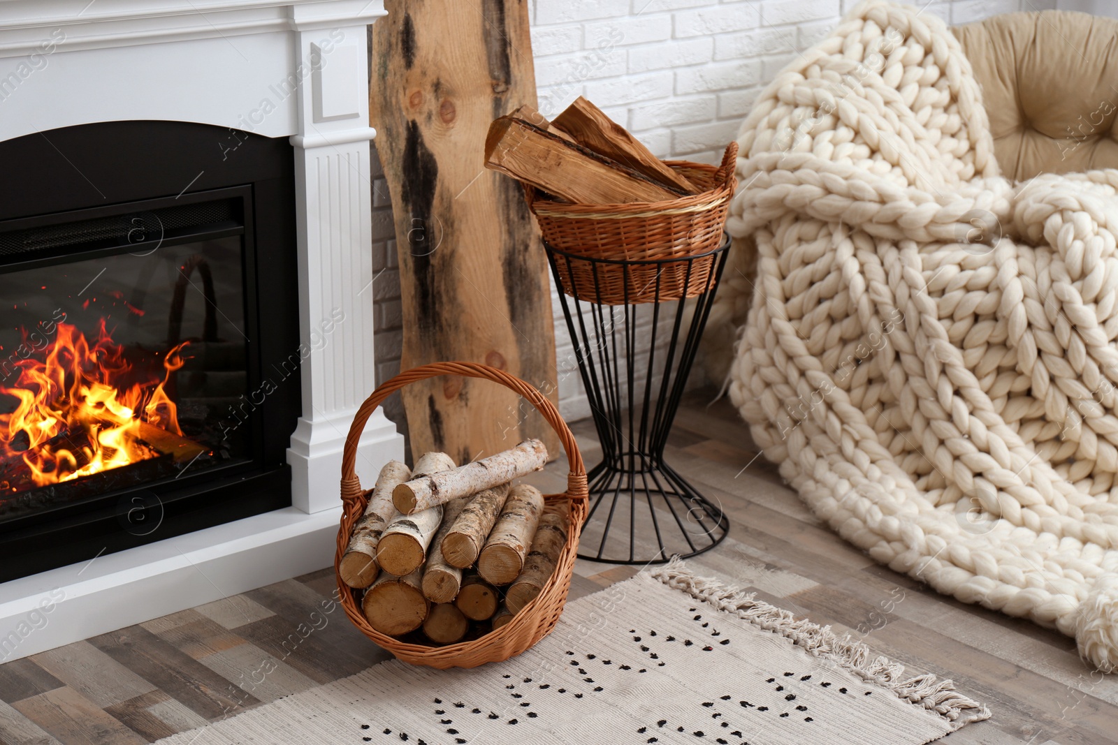 Photo of Wicker baskets with firewood and burning fireplace in cozy living room