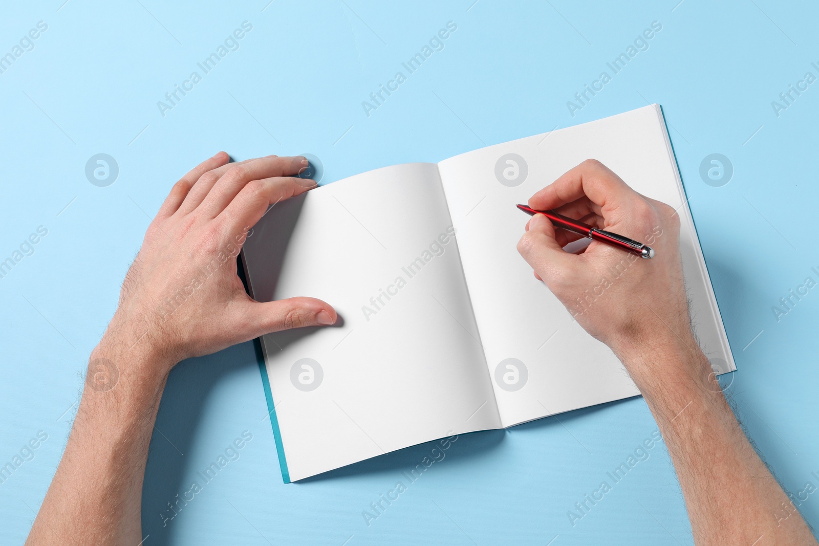 Photo of Man with pen and empty notepad on light blue background, top view