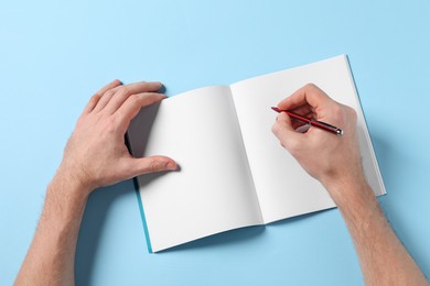 Man with pen and empty notepad on light blue background, top view