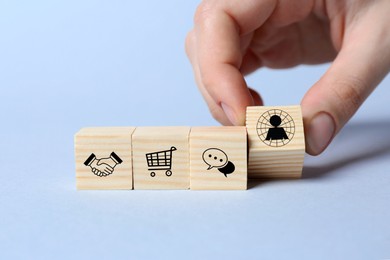 Professional buyer. Woman putting wooden cube with human icon on light background, closeup