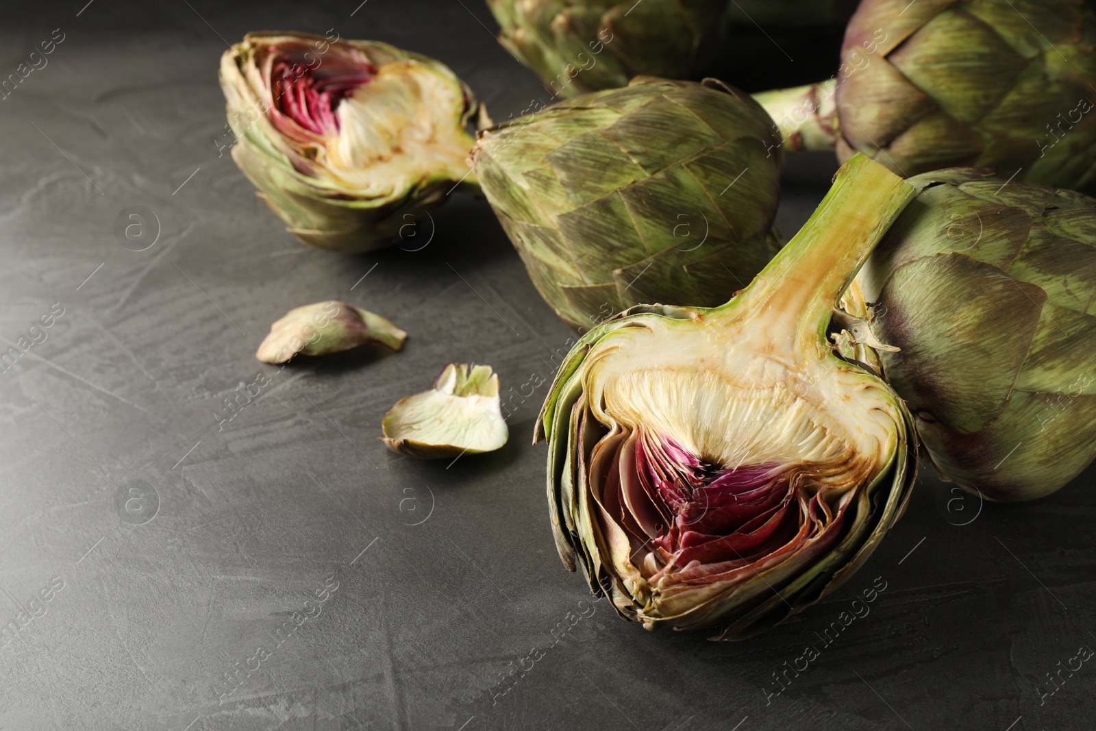 Photo of Cut and whole fresh raw artichokes on grey table, space for text