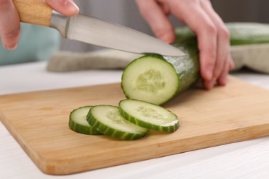 Photo of Woman cutting cucumber on wooden board at white table, closeup