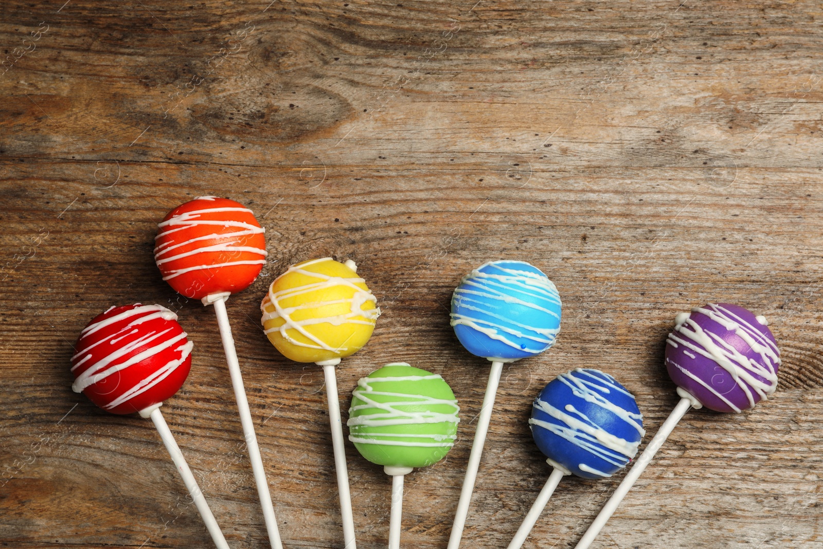 Photo of Bright delicious cake pops on wooden table, flat lay. Space for text