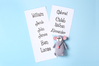 Photo of Lists of different baby names and toy on light blue background, flat lay