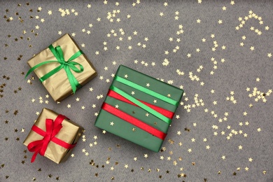 Photo of Christmas gift boxes and shiny confetti on grey background, flat lay. Space for text