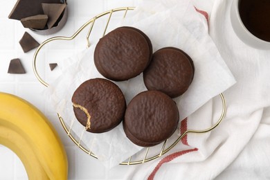 Tasty banana choco pies, pieces of chocolate and fruits on white tiled table, flat lay