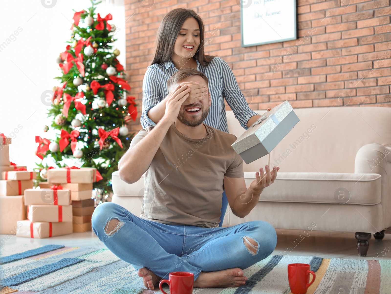 Photo of Young woman surprising her boyfriend with Christmas gift at home