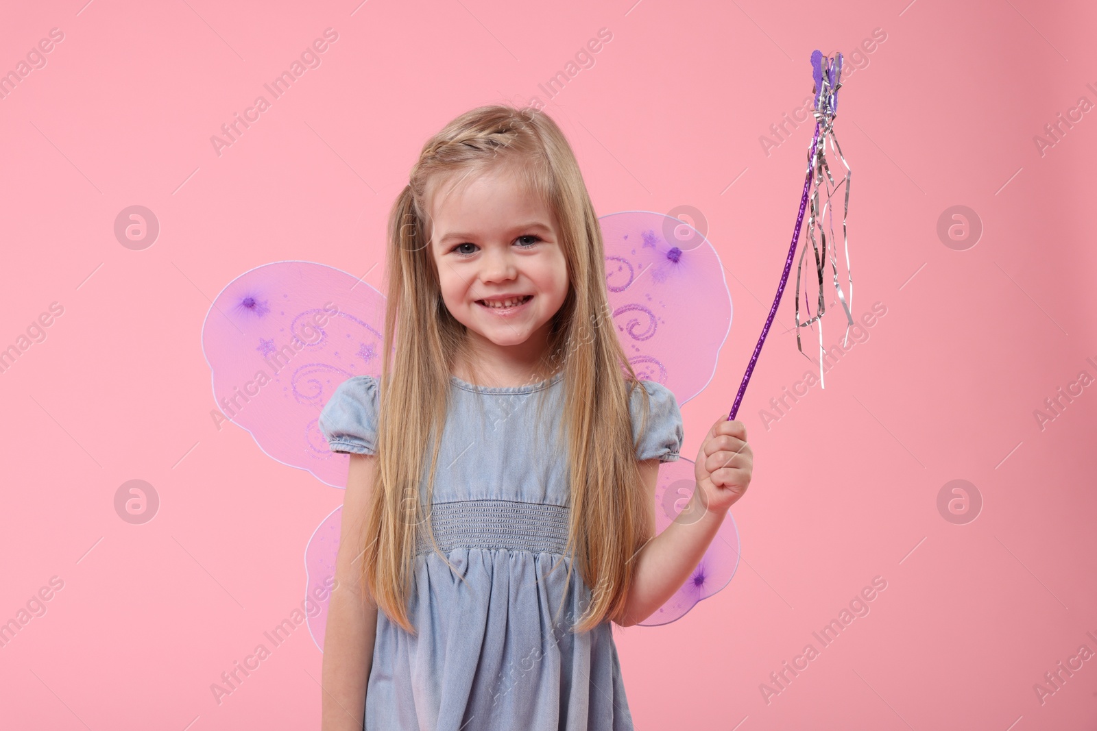 Photo of Cute little girl in fairy costume with violet wings and magic wand on pink background