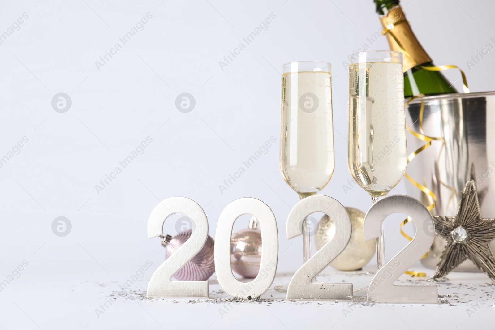 Photo of Happy New Year 2022! Bottle of sparkling wine in bucket and glasses on white background