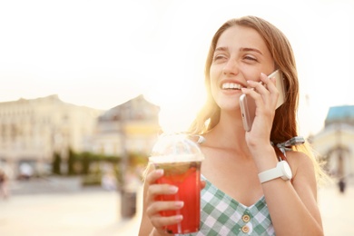 Photo of Young woman with refreshing drink talking on phone outdoors. Space for text