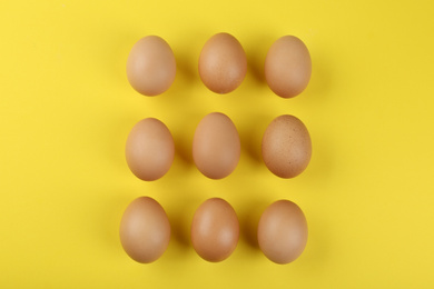 Raw chicken eggs on yellow background, flat lay