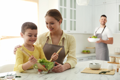 Photo of Happy family cooking salad together in kitchen