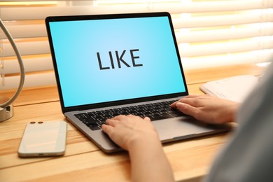 Image of Woman using laptop with word Like on screen at wooden table, closeup