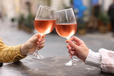 Women clinking glasses with rose wine at dark marble table in outdoor cafe, closeup