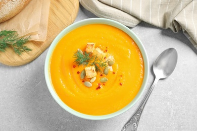 Delicious pumpkin soup in bowl on grey table, flat lay