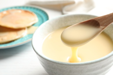 Spoon of pouring condensed milk over bowl on table, closeup with space for text. Dairy products