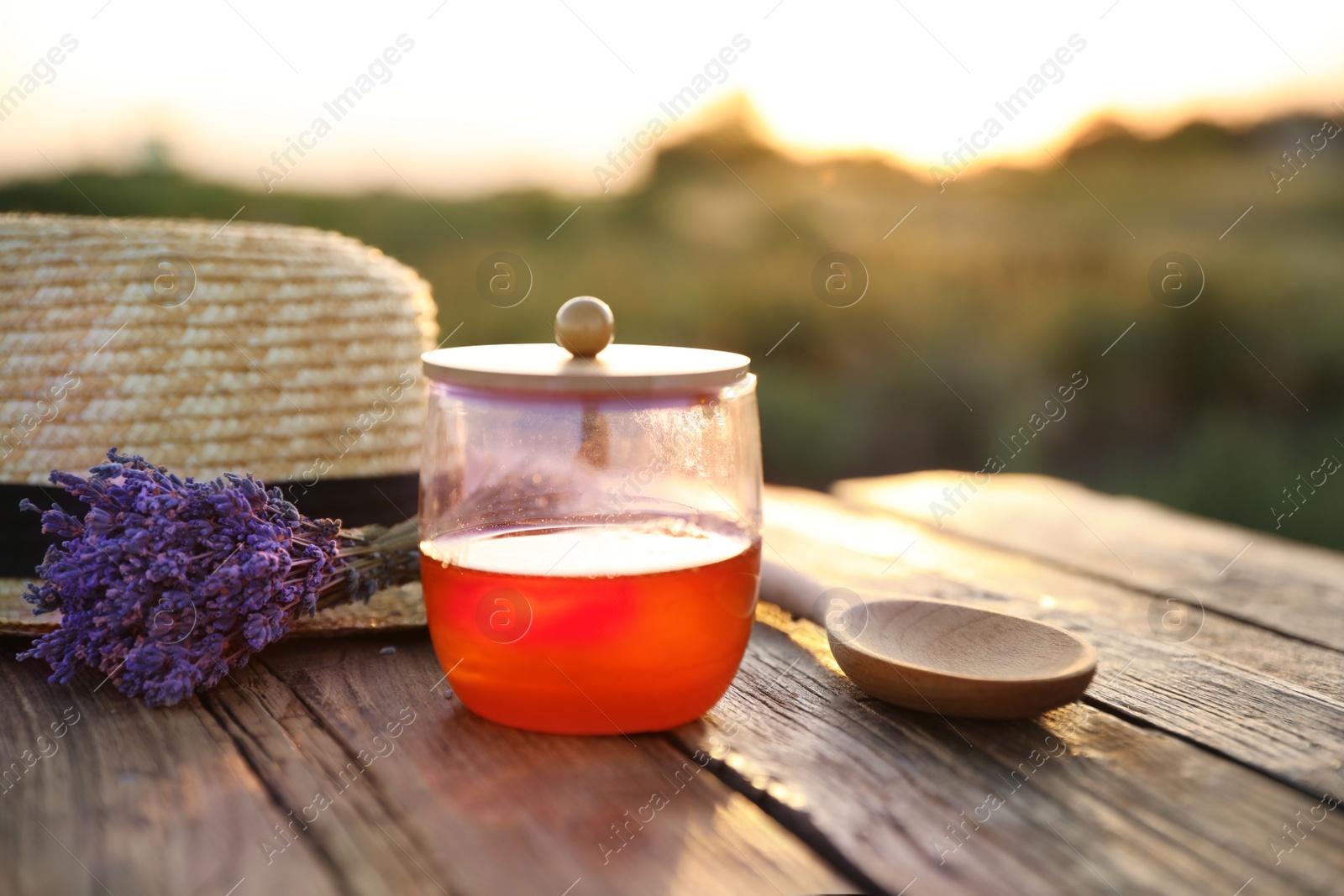 Photo of Jar with fresh honey and lavender flowers on wooden table outdoors