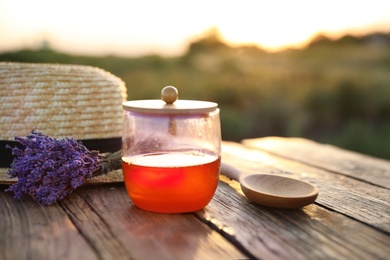 Jar with fresh honey and lavender flowers on wooden table outdoors