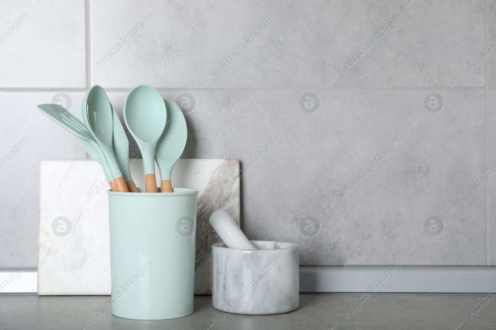 Photo of Set of kitchen utensils, mortar with pestle and cutting board on grey table. Space for text