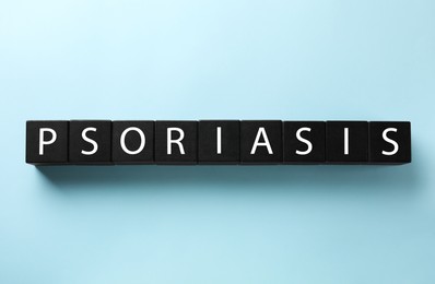 Photo of Word Psoriasis madeblack wooden cubes with letters on light blue background, top view