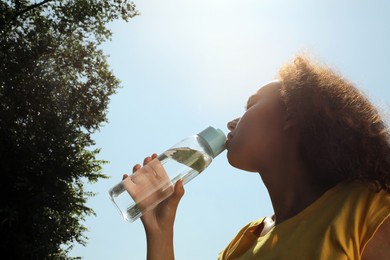 Photo of African-American woman drinking water to prevent heat stroke outdoors