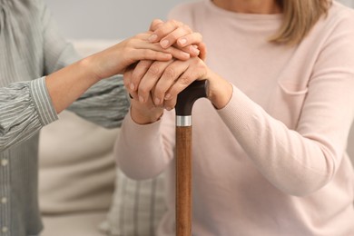 Photo of Mature lady with walking cane and young woman indoors, closeup