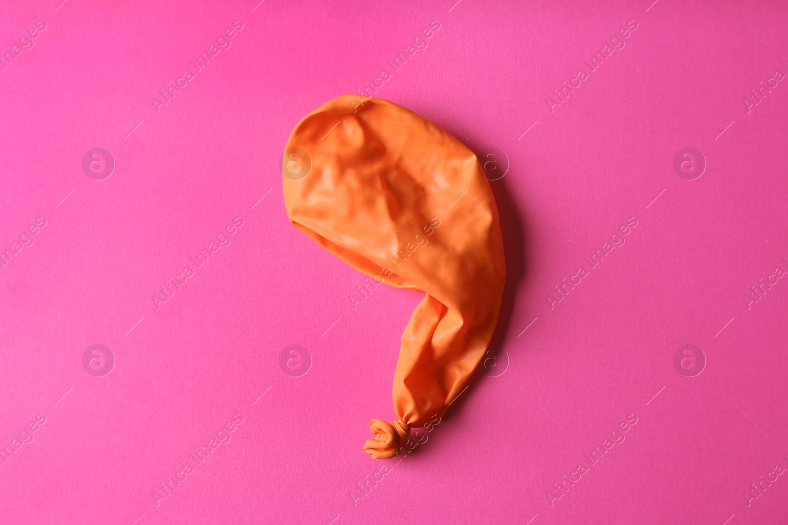 Photo of Orange deflated balloon on color background, top view