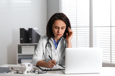 Photo of Doctor with headset and laptop consulting patient online in office. Hotline service