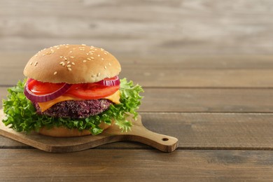 Photo of Tasty vegetarian burger with beet patty on wooden table. Space for text