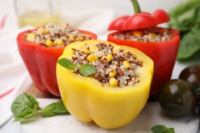 Photo of Quinoa stuffed bell peppers, basil and tomatoes on white table, closeup