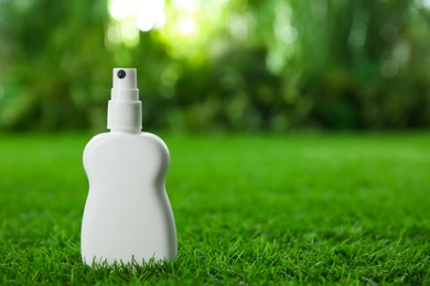 Photo of Bottle of insect repellent spray on green grass. Space for text