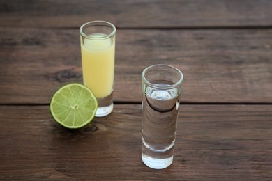 Shots with lime juice and Mexican tequila on wooden table. Traditional serving