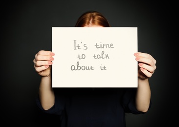 Photo of Young woman holding card with words IT'S TIME TO TALK ABOUT IT against dark background