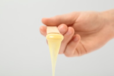 Photo of Woman holding spatula with hot depilatory wax on light  background, closeup