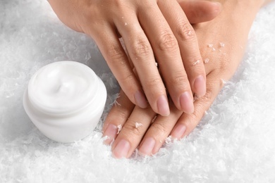 Photo of Woman holding hands near jar of cream on decorative snow. Winter skin care cosmetic