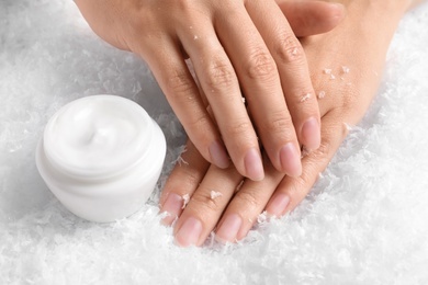 Woman holding hands near jar of cream on decorative snow. Winter skin care cosmetic