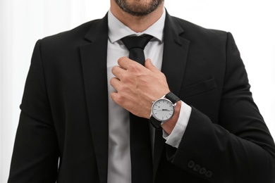 Photo of Businessman adjusting necktie on light background, closeup