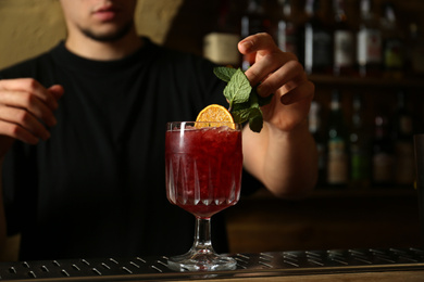 Photo of Bartender decorating glass of fresh alcoholic cocktail at bar counter, closeup