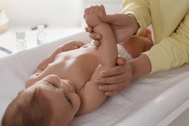 Mother massaging her baby with oil on changing table at home, closeup