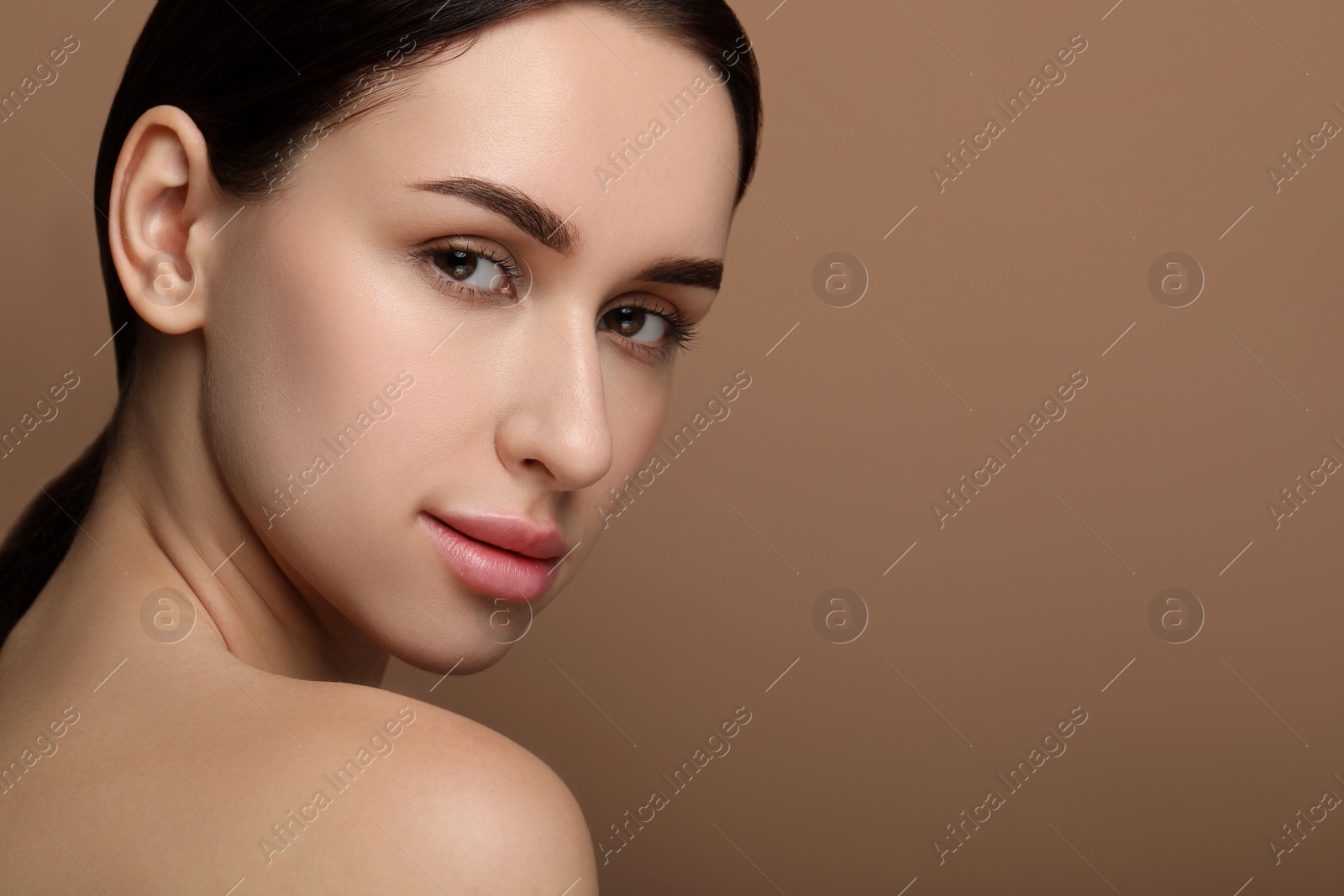 Photo of Beautiful young woman with healthy skin on brown background. Space for text