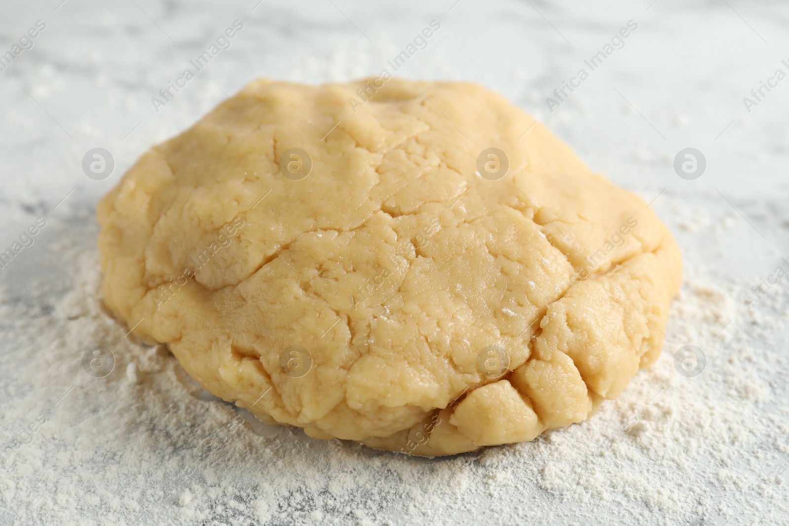 Photo of Making shortcrust pastry. Raw dough and flour on table, closeup