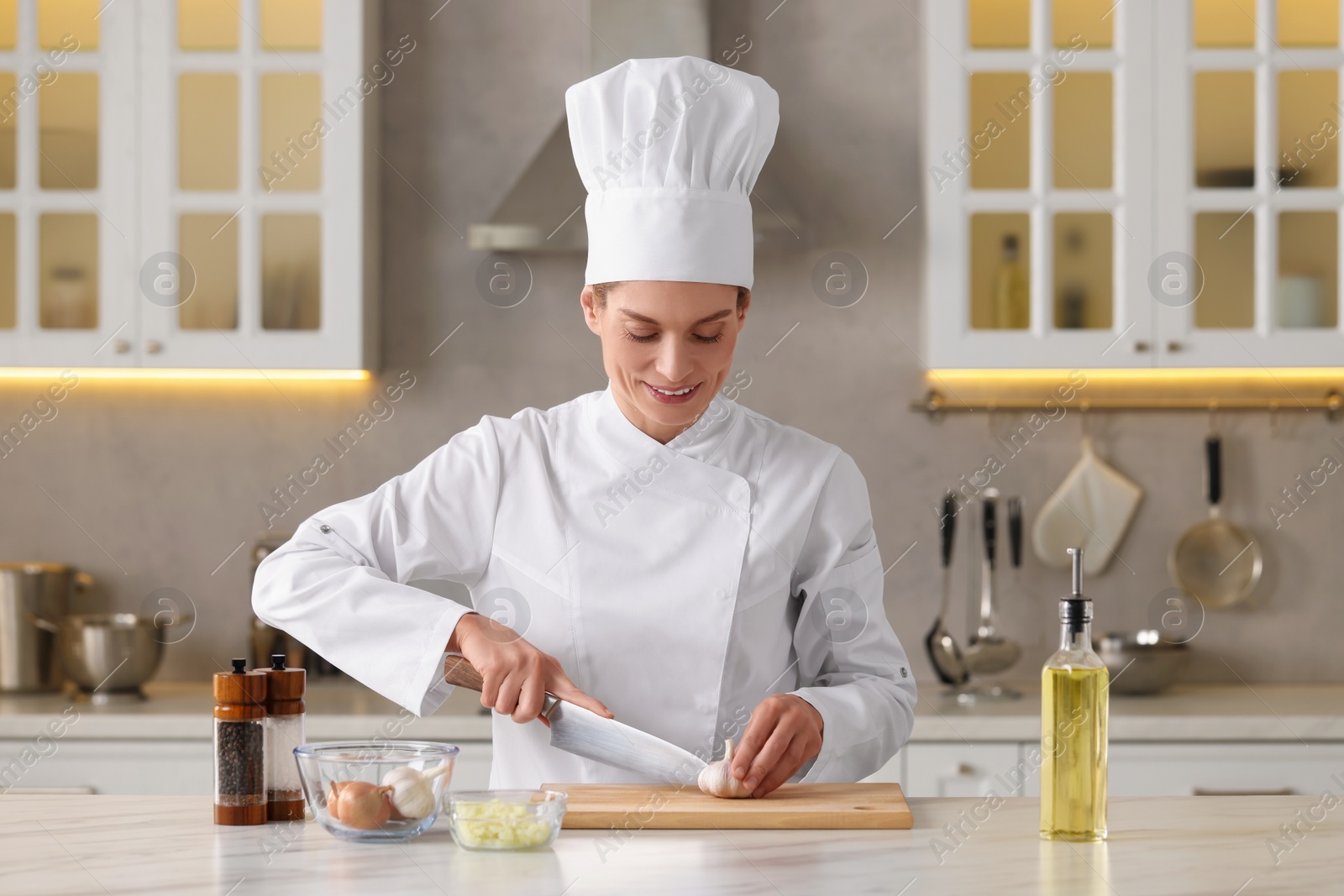 Photo of Professional chef cutting garlic at white marble table indoors