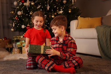 Photo of Cute little children with gift box near Christmas tree at home