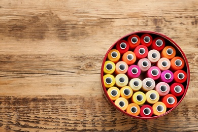 Container with set of color sewing threads on wooden background