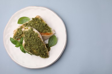 Delicious chicken breasts with pesto sauce and basil on light gray table, top view. Space for text