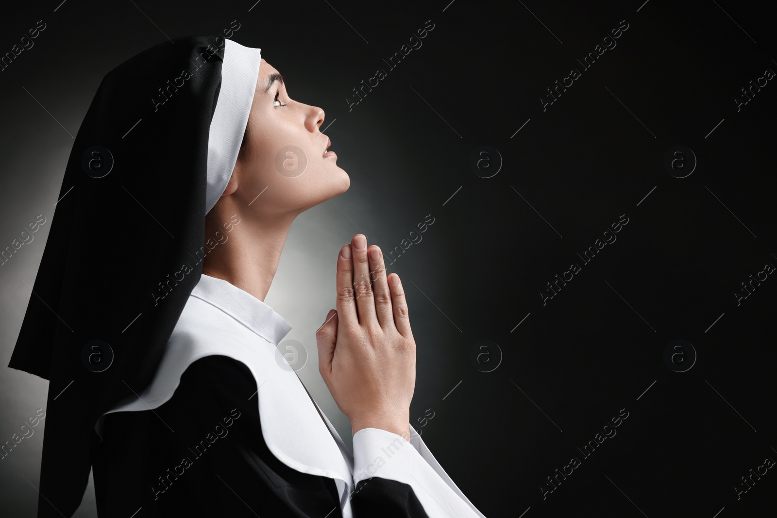 Photo of Nun with clasped hands praying to God on black background. Space for text